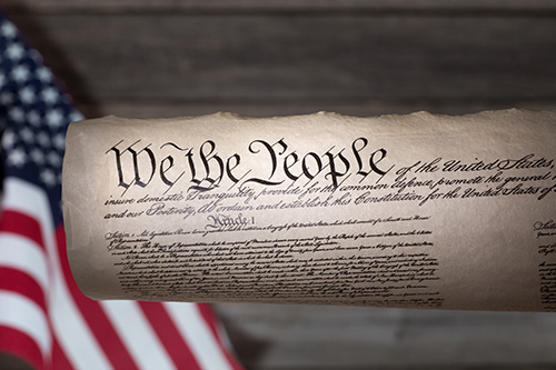Photo of a rolled up US Constitution with an American Flag in the background