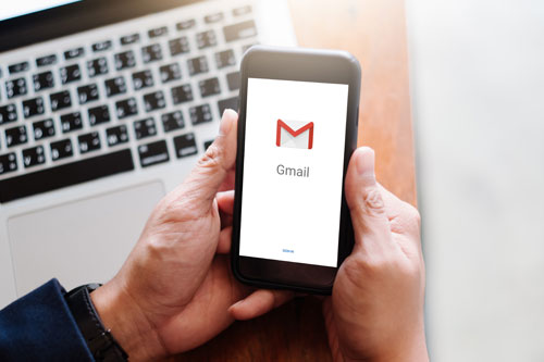 Hands using a phone that has the gmail logo on the screen
